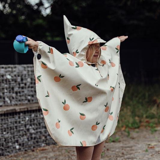 Kind mit Orangen-Regenponcho und Magnetknöpfen breitet die Arme aus, Outdoor-Szene im Regen.