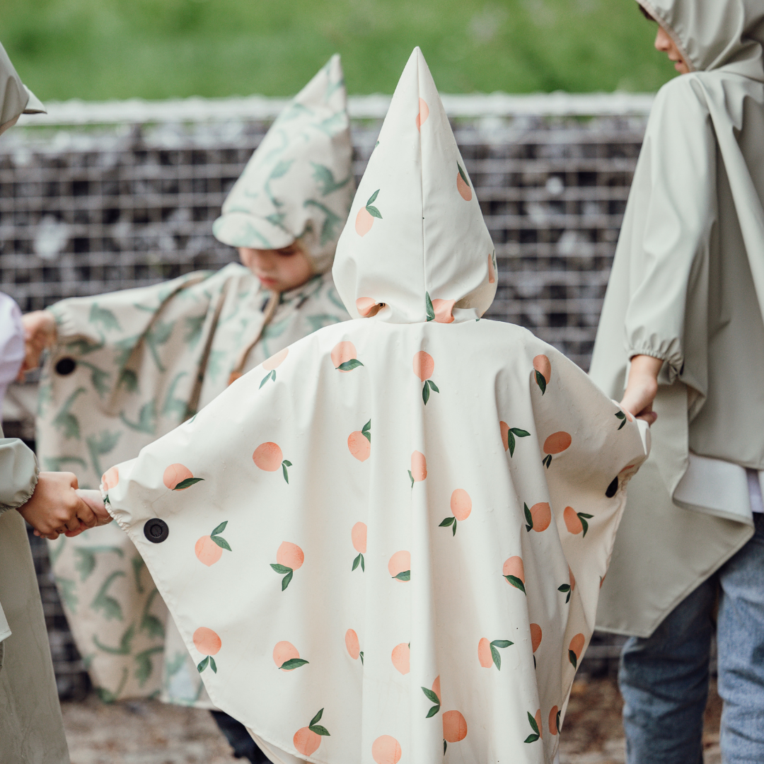 Rückansicht mehrerer Kinder mit farbenfrohen Ponchos – Fokus auf Zipfelkapuze und Magnetknopf-Ärmel.