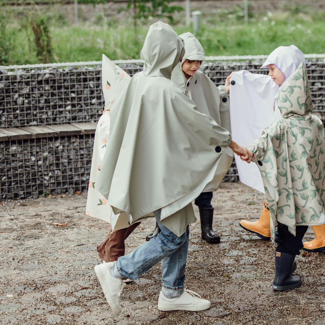 Kinder spielen im Kreis mit Ponchos in verschiedenen Farben – wasserabweisende Stoffe mit Magnetknöpfen sichtbar an den Armen.