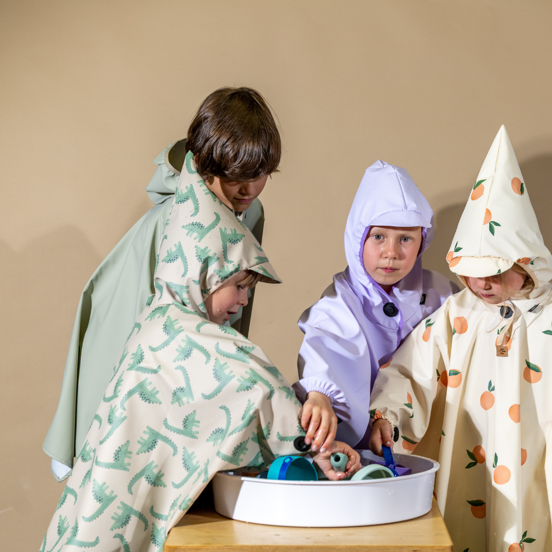 Vier Kinder in farbenfrohen Regenponchos beim Spielen – vielseitige Regenkleidung für Alltag, Fahrrad und Kita