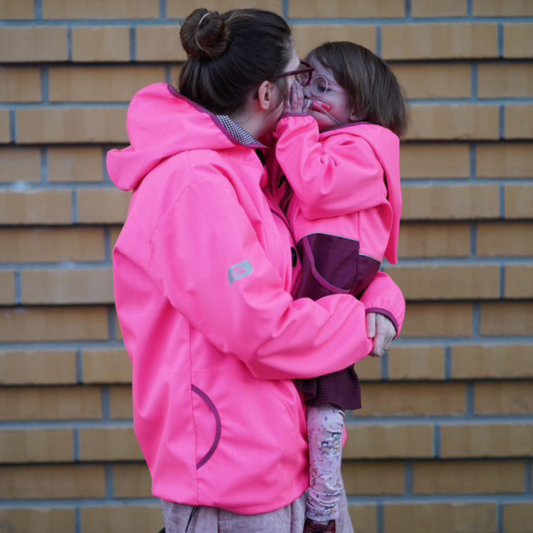 Mama mit Kind auf dem Arm, beide in pinker Wetterheldenjacke