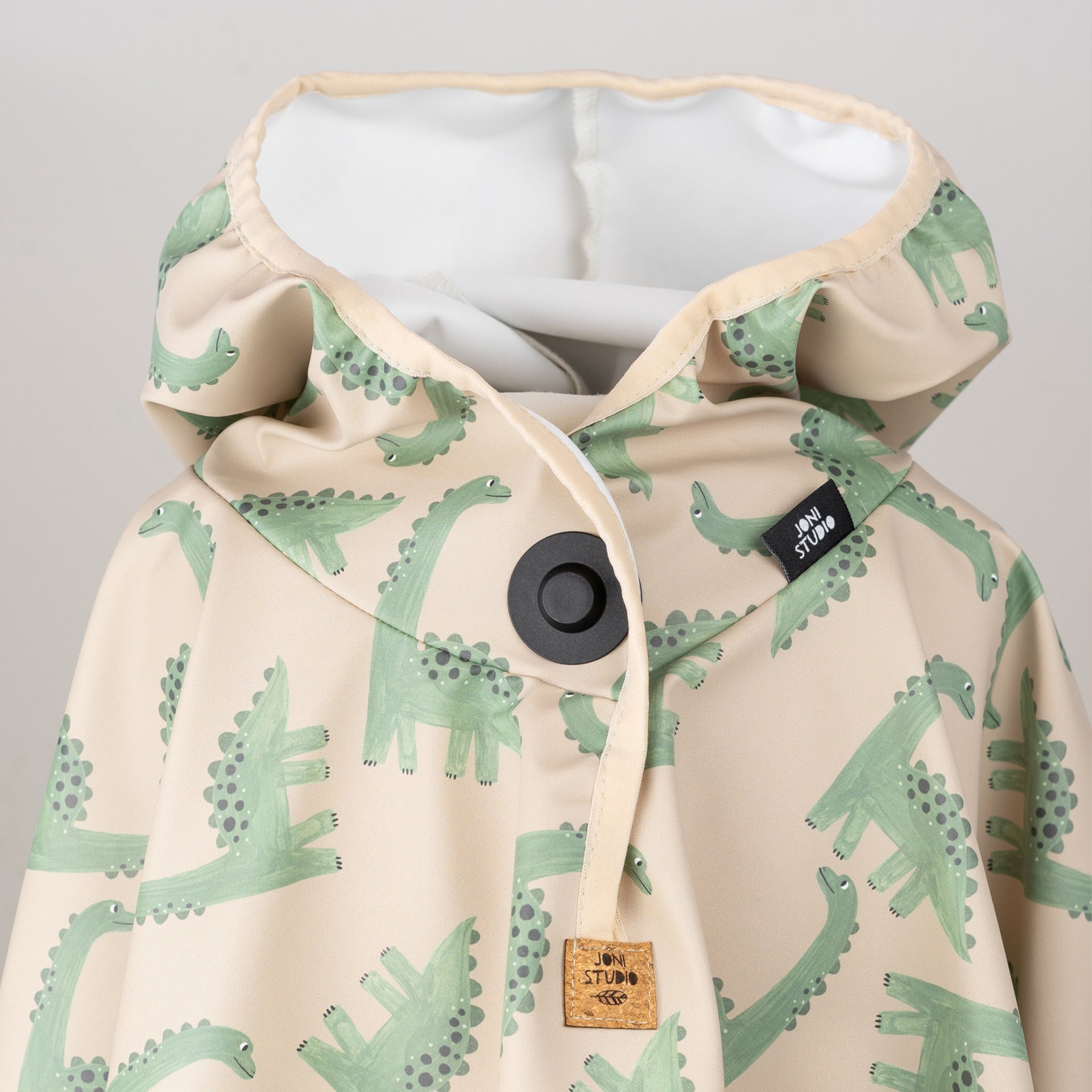 Kinder-Regenponcho mit Kapuze und grünem Dino-Print – Detailansicht mit Joni Studio Label und Magnetknopf